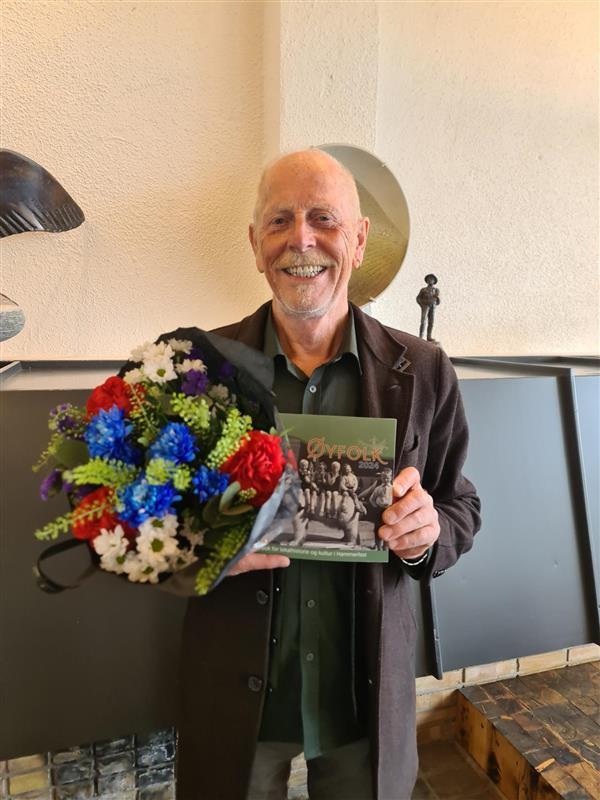 Mann med grønn skjorte og svart jakke, holder blomsterbukett og viser frem boka &quot;Øyfolk&quot; - Klikk for stort bilde