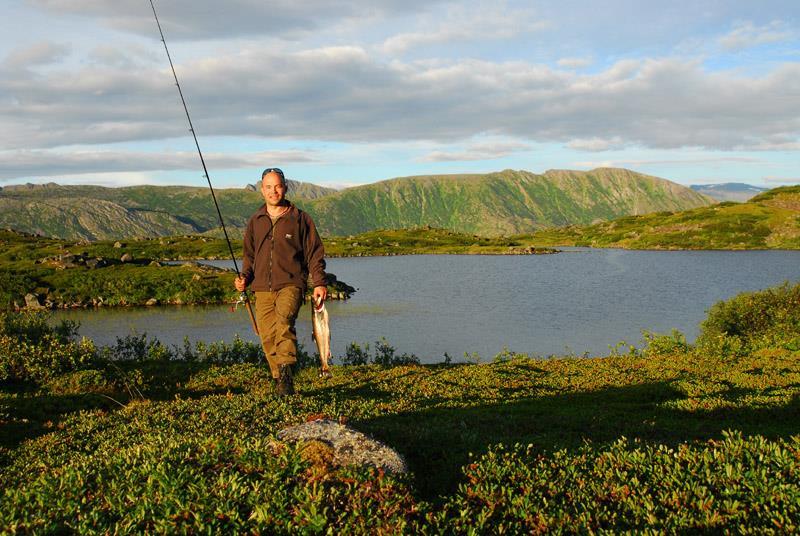Mann med fiskestang og fisk foran fiskevann - Klikk for stort bilde